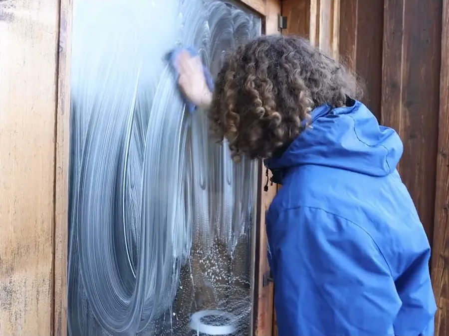 A Camelot window cleaner hand-washing an exterior window, soap still on the glass